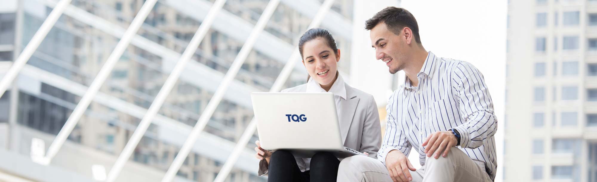 Mann und Frau sitzen mit TQG Laptop auf Treppe